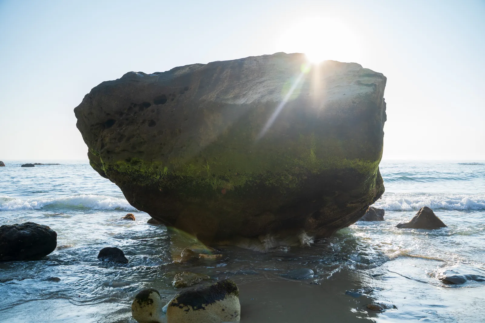 Mushroom-shaped sea rock with the sun cresting its edge into a clean sunstar