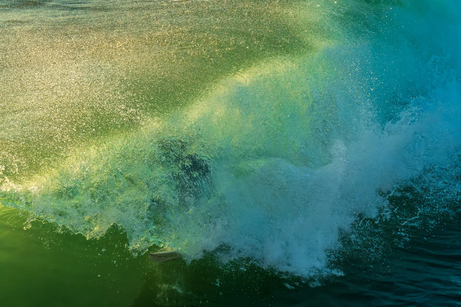 Empty wave breaking, shot tight and low: backlit teal-to-green curl with the lip throwing spray across the top third. No subject needed, no horizon clutter, no sky to blow out. Reads as a deliberate water study rather than a snapshot
